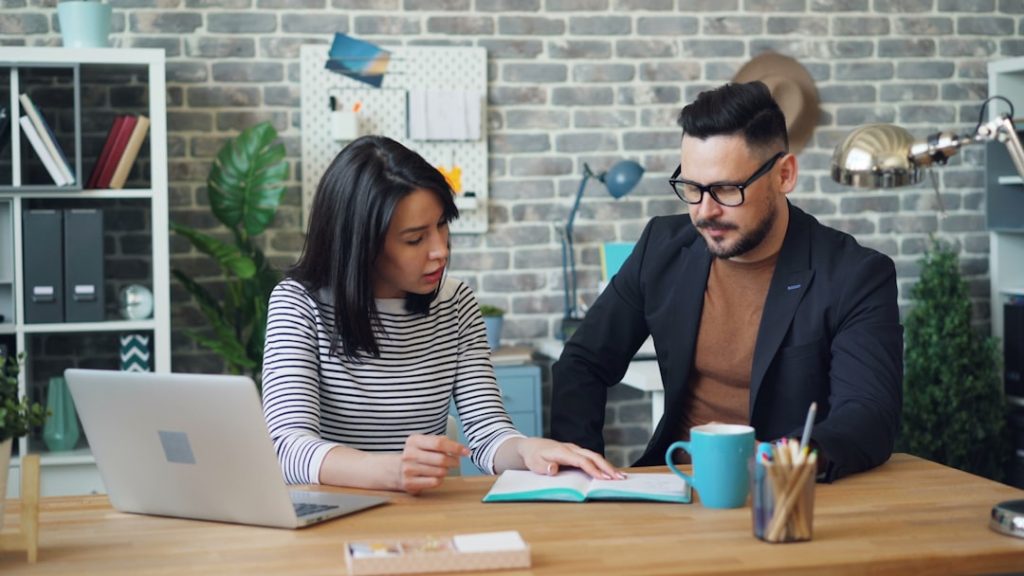 A coach and client sitting together at a table reviewing session notes on a laptop, illustrating where AI coaching software fits around the coaching conversation.