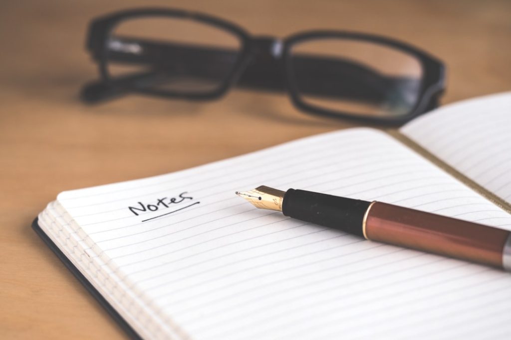 A fountain pen resting on an open notebook, evoking the note-taking a coach does after a client session.