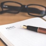 A fountain pen resting on an open notebook, evoking the note-taking a coach does after a client session.