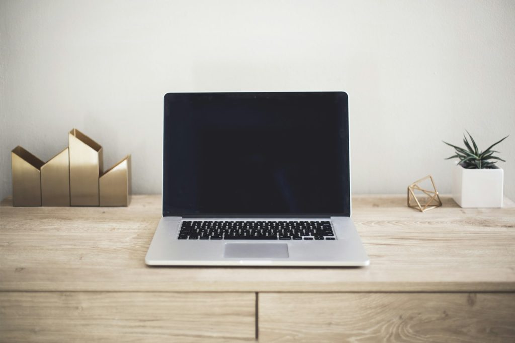A laptop and notebook on a wooden desk, the workspace a life coach uses to run their coaching practice