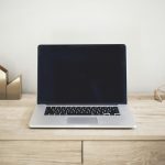 A laptop and notebook on a wooden desk, the workspace a life coach uses to run their coaching practice