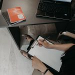 Organizing client notes on a clipboard beside a laptop.
