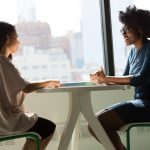A coach and client in a focused one-on-one conversation across a table, the kind of session an online coaching platform is built to support.