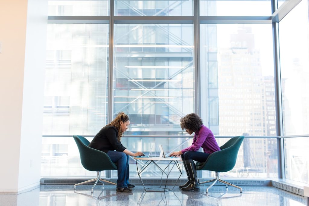 Two people sitting side by side with open laptops, comparing coaching platforms together the way a coach evaluates software before committing.