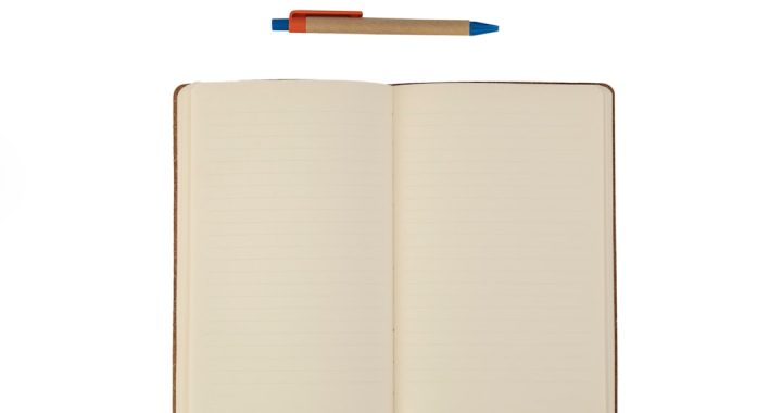 An open blank notebook with cream lined pages lying flat, a kraft-paper ballpoint pen with blue and orange trim resting above it, on a plain white background.