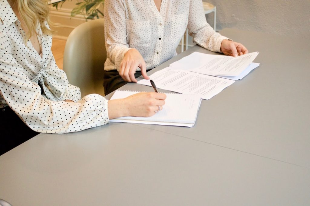 Two women seated across a table reviewing and signing paperwork together, the moment a coaching prospect becomes a client.