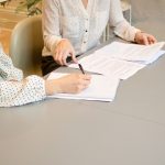 Two women seated across a table reviewing and signing paperwork together, the moment a coaching prospect becomes a client.