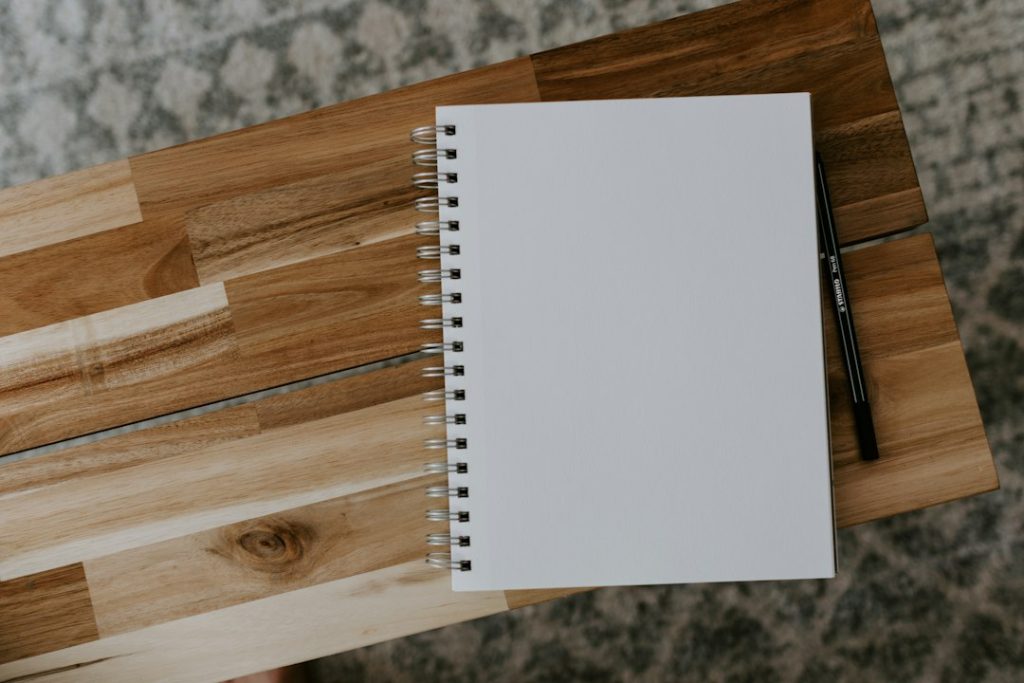 A blank spiral notebook and a black pen on a wooden table, seen from above