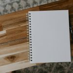 A blank spiral notebook and a black pen on a wooden table, seen from above