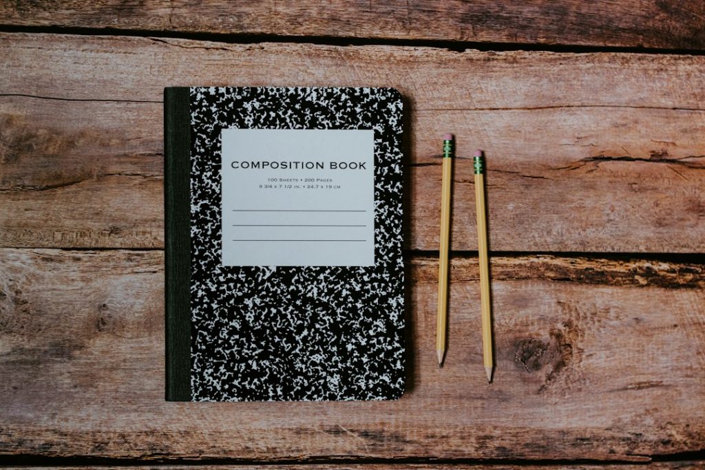 A black-and-white composition notebook and two sharpened pencils on a weathered wooden table, seen from above