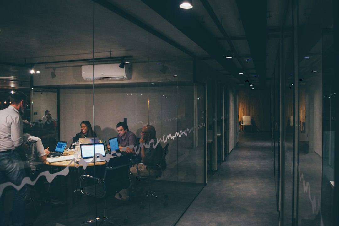 Four people working together around a small table with laptops in a glass-walled office at night