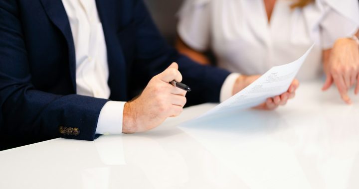 Two people at a white table reviewing a printed document, one holding a pen over the page