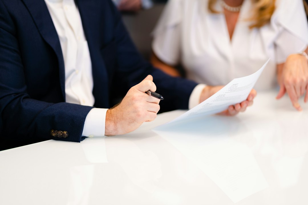Two people at a white table reviewing a printed document, one holding a pen over the page