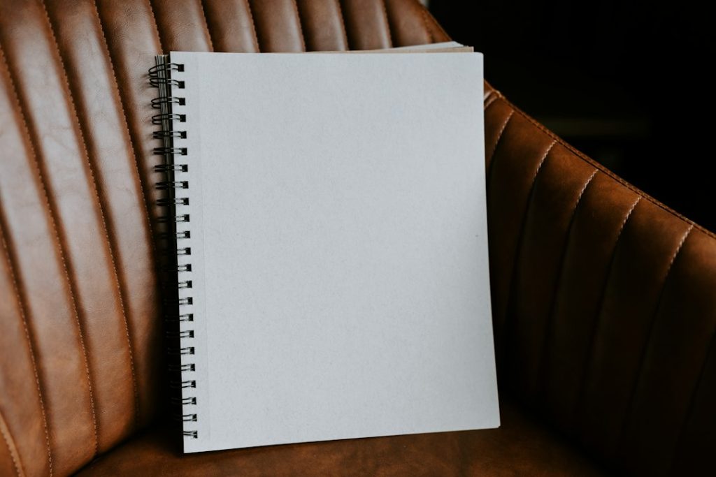 A blank spiral-bound notebook resting upright on a brown leather armchair