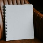 A blank spiral-bound notebook resting upright on a brown leather armchair